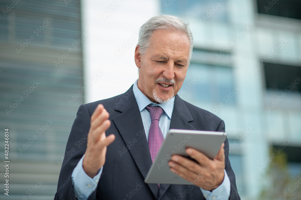 Senior businessman using his tablet in a city Senior businessman using his tablet in a city