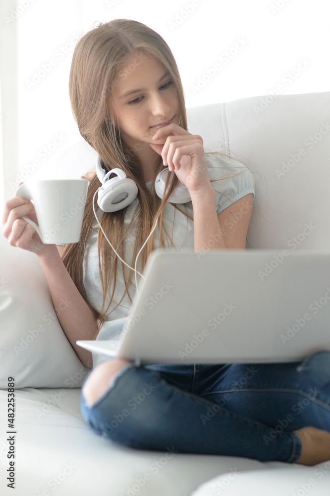 Cute girl with headphones using laptop on sofa at home Cute girl with headphones using laptop on sofa at home