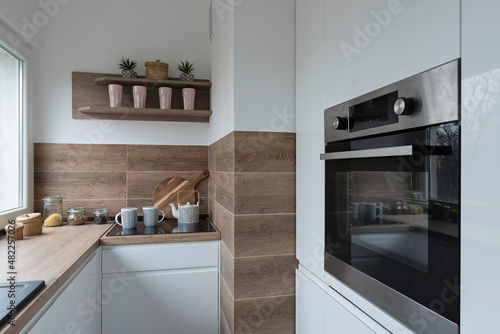 Modern interior of kitchen with white furniture, oven and stylish tiles on the wall. Wooden counter and design decor.