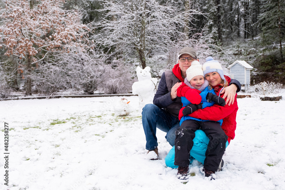 Happy family of Caucasians, smiling and looking at the camera. Man, woman and child 5 years old make a snowman. Fun and happiness with family.