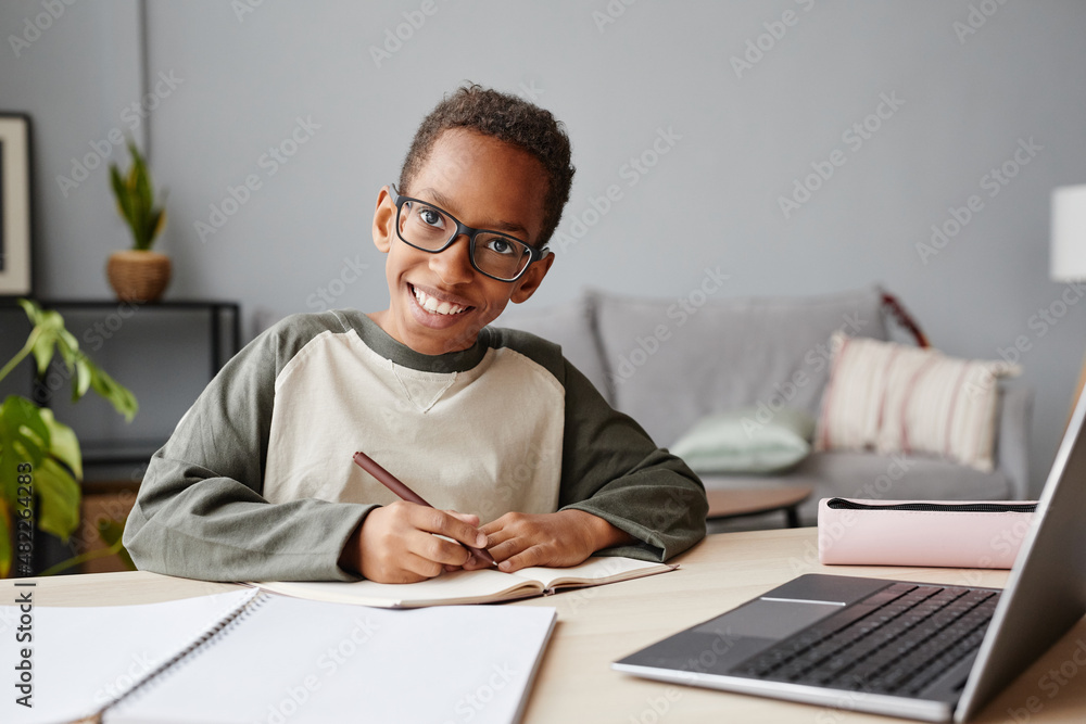 Fototapeta premium Portrait of smiling African-American boy wearing glasses while studying at home, homeschooling concept, copy space