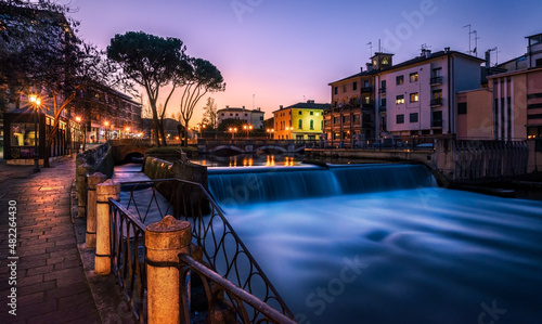 Treviso, the San Martino Bridge at sunset. On the right a little waterfall on the Sile river, on the left a walk illuminated by street lamps