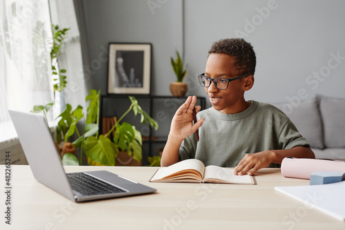 Portrait of smiling African-American boy wearing glasses watching online lessons while studying at home, homeschooling concept, copy space