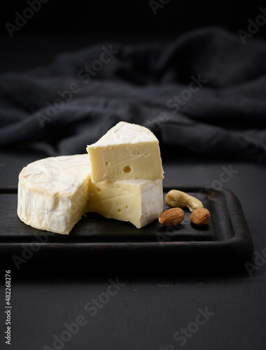 round brie cheese on brown wooden cutting board, black background photo