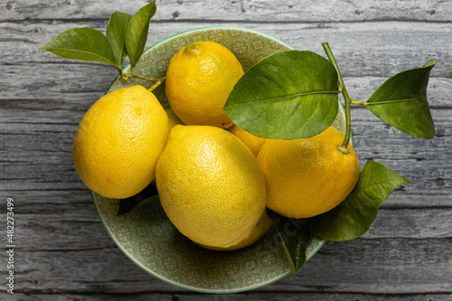 Zenital shot of a fruit bowl full of fresh and organic lemons without chemical treatment. The bowl stands on an old wooden surface