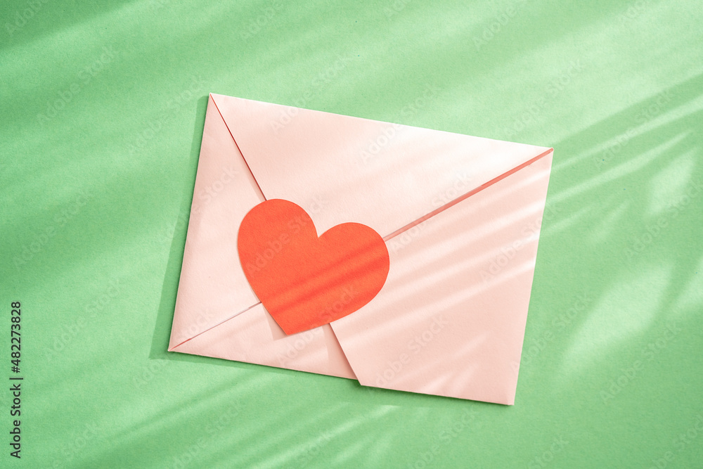 Love envelop with red heart on green natural background. Vanetines Day celebration. Natural shadows Love envelop with red heart on green natural background. Vanetines Day celebration. Natural shadows