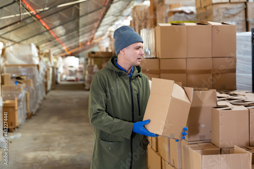 Storekeeper man stacking pasteboard box in storehouse during working day.