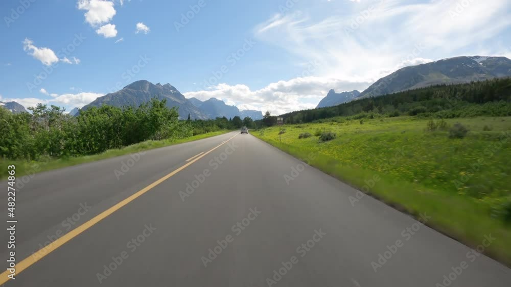 Riding a car on asphalt mountain road in Glacier National Park, Montana. Sunny day with blue sky and white clouds Riding a car on asphalt mountain road in Glacier National Park, Montana. Sunny day with blue sky and white clouds
