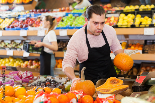 Young man with pumpkin in hands wearing apron on the supermarket