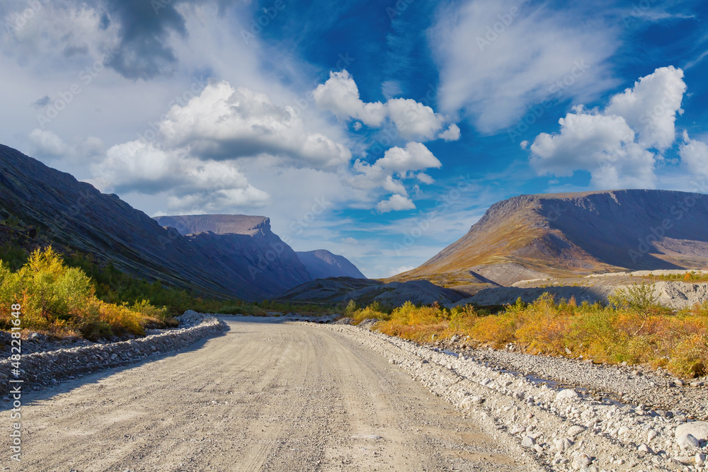 Dirt road. Highway in picturesque place. Not paved road for cars. Suburban landscape. Mountains on background of blue sky. Wide winding path leads into gorge. Path to natural gorge