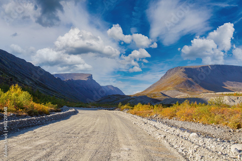 Dirt road. Highway in picturesque place. Not paved road for cars. Suburban landscape. Mountains on background of blue sky. Wide winding path leads into gorge. Path to natural gorge