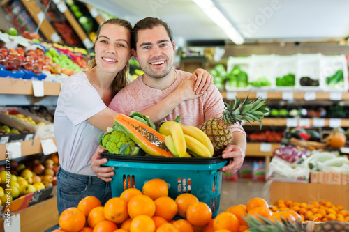 Young family couple standing with full grocery cart after shopping in fruit store