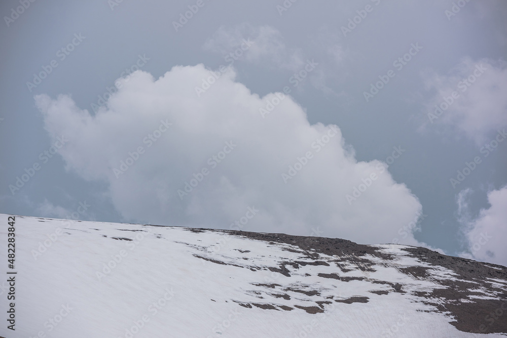Atmospheric alpine landscape with high snow mountain wall under rainy clouds in gray sky. Dramatic overcast scenery with large snowy mountain top under gray cloudy sky. Gloomy weather at high altitude Atmospheric alpine landscape with high snow mountain wall under rainy clouds in gray sky. Dramatic overcast scenery with large snowy mountain top under gray cloudy sky. Gloomy weather at high altitude