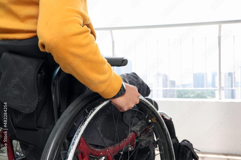 Obraz premium South east Asian malay middle aged disabled man on wheelchair looking sitting in front of balcony window look outside closeup hand