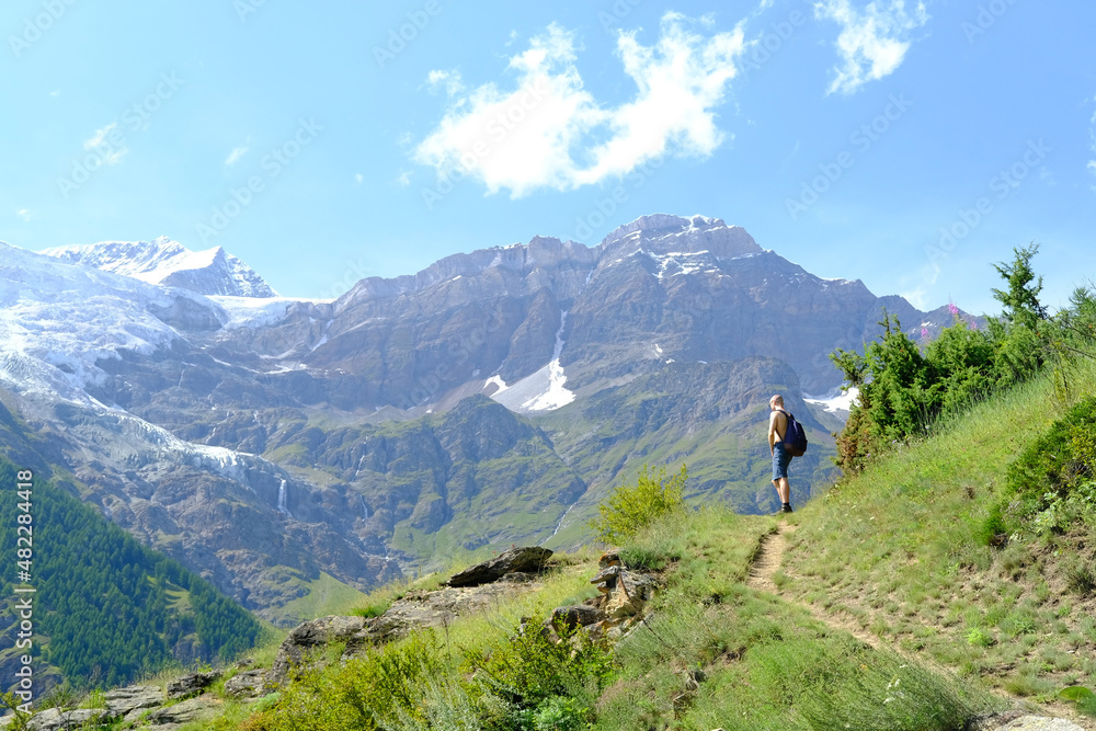 young tourist with backpack, man stands on mountain, Swiss Alps with snow-capped Matterhorn peak visible in background, concept of hiking, rock climbing, active lifestyle, beauty of nature
