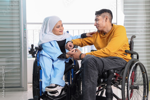 South east Asian malay man woman couple headscarf tudung middle aged disabled on wheelchair looking sitting in front of balcony window look happy love