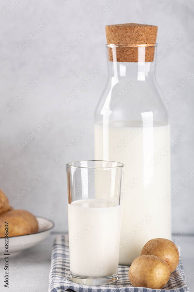 Dairy-free potato drink in glass and bottle. Alternative potato milk and potato tubers on gray table. Copy space Dairy-free potato drink in glass and bottle. Alternative potato milk and potato tubers on gray table. Copy space