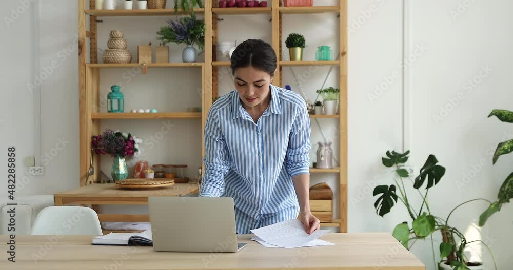 Attractive millennial businesslady stand in modern office, leaned over desk checking corporate paperwork correspondence, read documents, analyzing papers, prepare contract, make report at workplace Attractive millennial businesslady stand in modern office, leaned over desk checking corporate paperwork correspondence, read documents, analyzing papers, prepare contract, make report at workplace