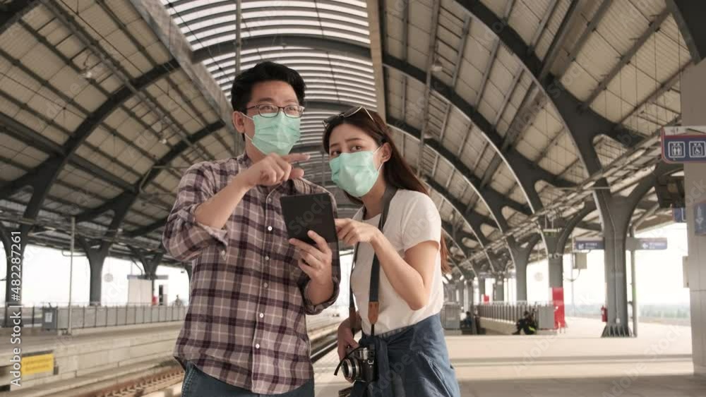 Face mask man helps Asian female tourist search information, find travel locations with tablet at public train station platforms, passenger trip lifestyles, casual journey vacation transportation. Face mask man helps Asian female tourist search information, find travel locations with tablet at public train station platforms, passenger trip lifestyles, casual journey vacation transportation.