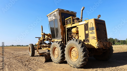 Graded on a new build road. Heavy equipment Grader is constructing a road or repair road on a blue sky background with copy space. Selective focus