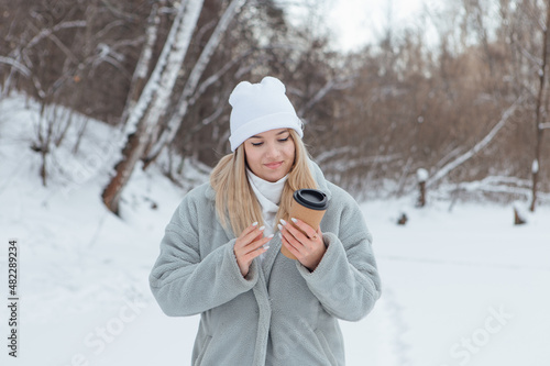 A beautiful young girl smiling and enjoying drinking coffee in a winter forest.