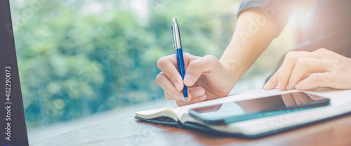 Woman hand writing on a notepad with a pen in the office.