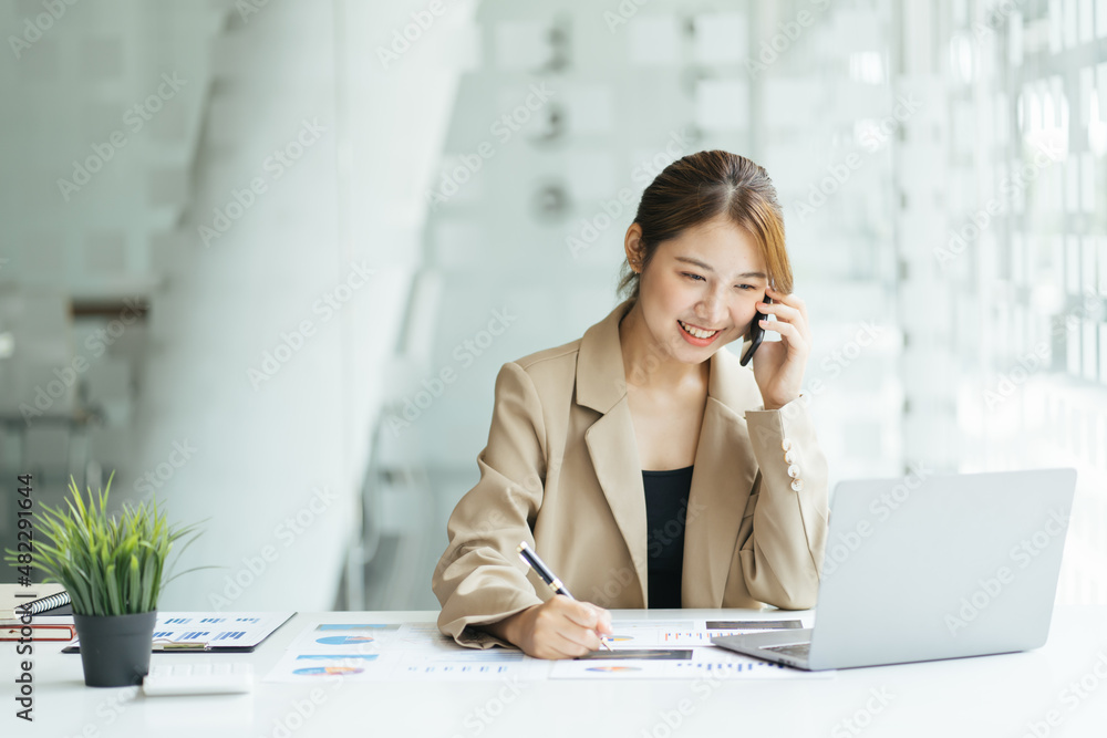 Overjoyed asian female laughing telling funny story by phone to friend colleague sitting by office computer screen. Young woman enjoying conversation by cell discussing good positive news. Overjoyed asian female laughing telling funny story by phone to friend colleague sitting by office computer screen. Young woman enjoying conversation by cell discussing good positive news.
