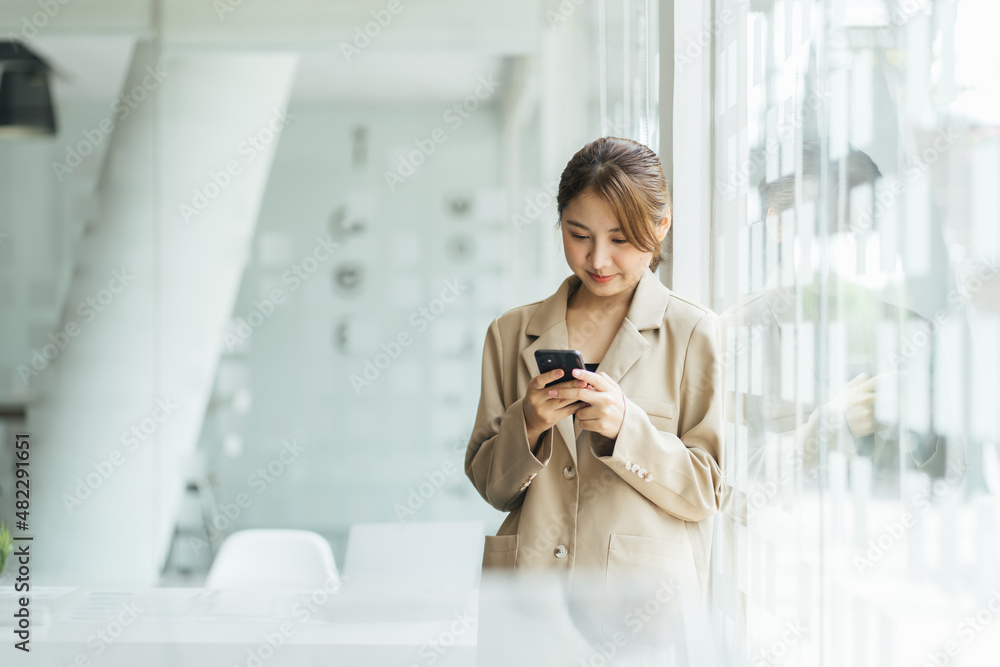 Fototapeta premium Asian woman with smartphone standing against street blurred building background, Fashion business photo of beautiful girl in casual suite with smart phone.