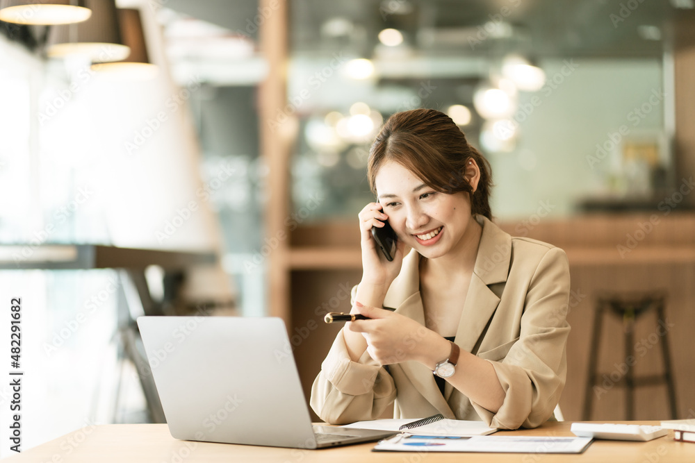 © PaeGAG - Photo of a young cheerful happy woman in office using laptop computer talking by mobile phone.