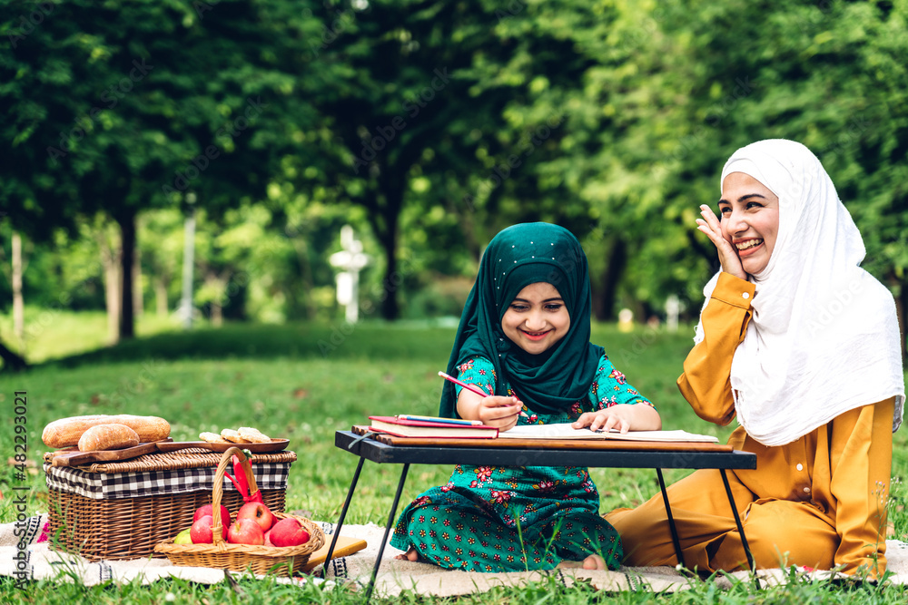Portrait happy love asian muslim family mother teach little daughter muslim girl learn and study.Mom and muslim girl writing with book and pencil making lessons in green park.Education Portrait happy love asian muslim family mother teach little daughter muslim girl learn and study.Mom and muslim girl writing with book and pencil making lessons in green park.Education