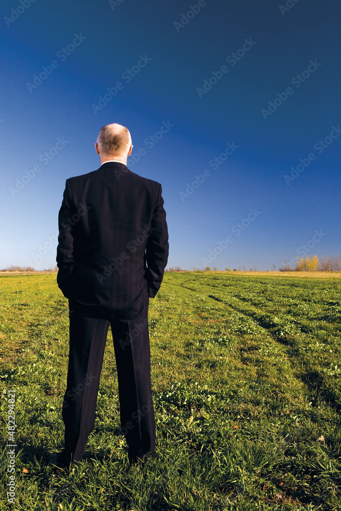Homem de terno preto em pé observando o campo.