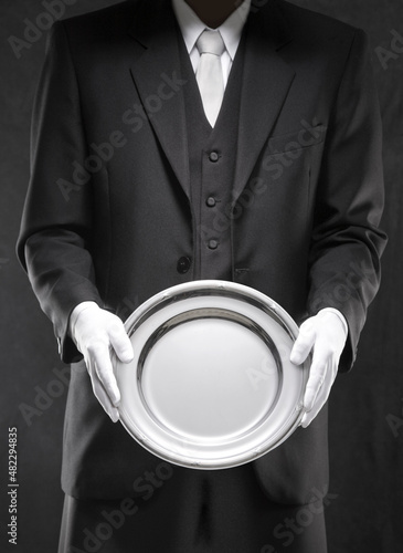 Mordomo usando terno com luvas brancas segurando um prato. (ID: 482294835)