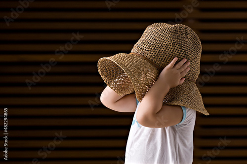 Criança de perfil cobrindo a cabeça com um chapéu de palha. (ID: 482294865)