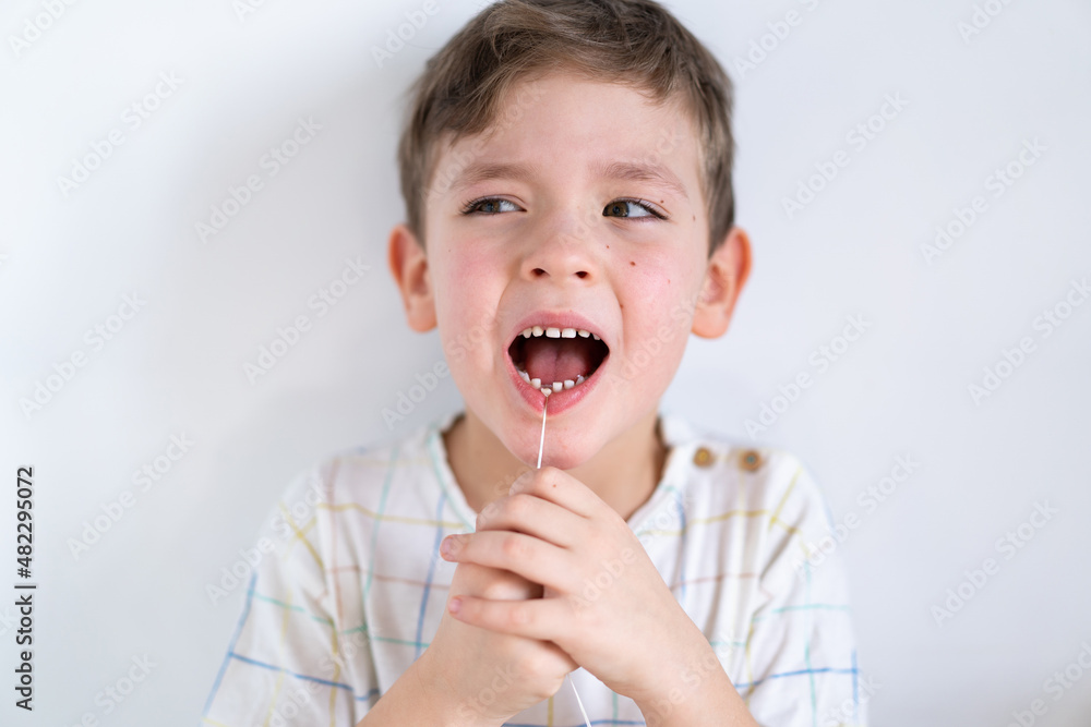 Cute boy pulling loose tooth using a dental floss. The boy's first milk