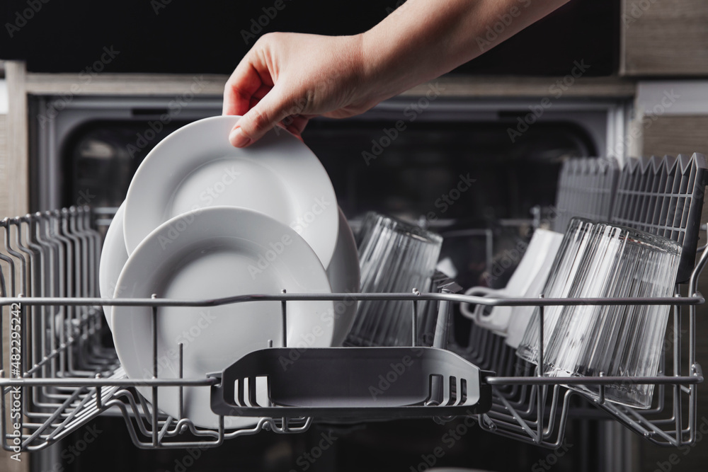 Female hand loading dished, empty out or unloading dishwasher with