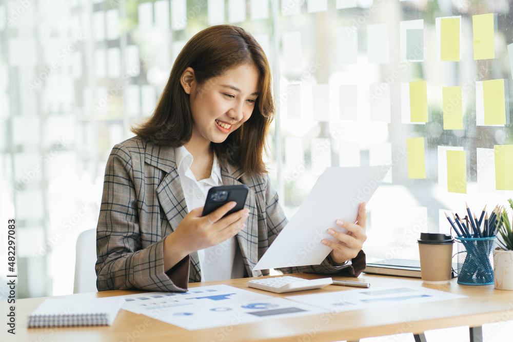 Female entrepreneur works and sits at workplace desk in office hold smartphone, prepare document agreement check details, read contract terms and conditions. Female entrepreneur works and sits at workplace desk in office hold smartphone, prepare document agreement check details, read contract terms and conditions.