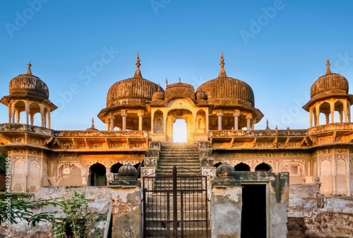 Street view of the front of an abandoned, dilapidated Indian haveli at sunrise in Mandawa, Rajasthan, with its ornate architecture and Shekhawati style painting still visible on the exterior walls. photo