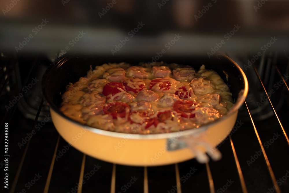 Homemade pizza with sausages, tomatoes and cheese in hot air oven close up with selective focus. Process of cooking pizza, step 11 Homemade pizza with sausages, tomatoes and cheese in hot air oven close up with selective focus. Process of cooking pizza, step 11