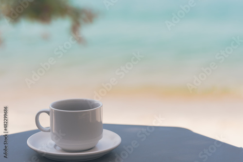 White coffee cup on gray table There is space on the side for design or product placement. beautiful sea and nature blur background, Relaxing and vacation concept, Samui Thailand beach.