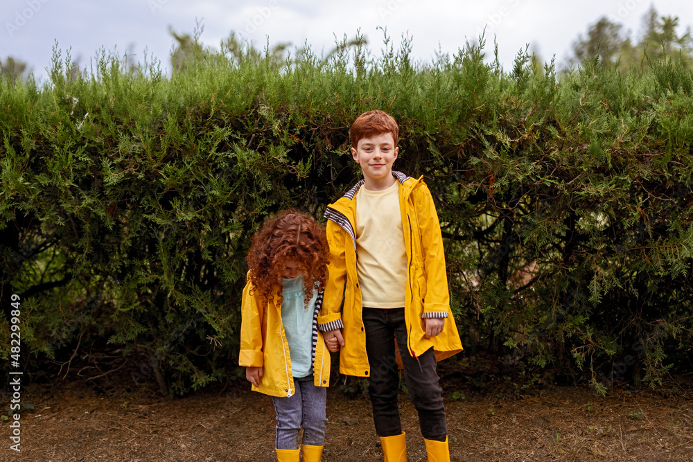 Fototapeta premium Redhead siblings in yellow raincoats in park