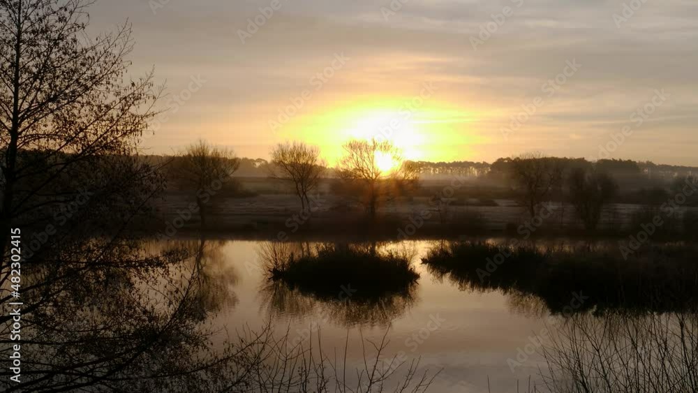 Sunrise over the Nunnery Lakes in Thetford, Norfolk, UK in timelapse. Beautiful rising sun over trees and lake in the countryside. Sunrise over the Nunnery Lakes in Thetford, Norfolk, UK in timelapse. Beautiful rising sun over trees and lake in the countryside.
