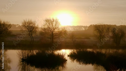 Scenic sunrise over the Nunnery Lakes in Thetford, Norfolk, UK. Rising sun over the trees and lake in the countryside. photo