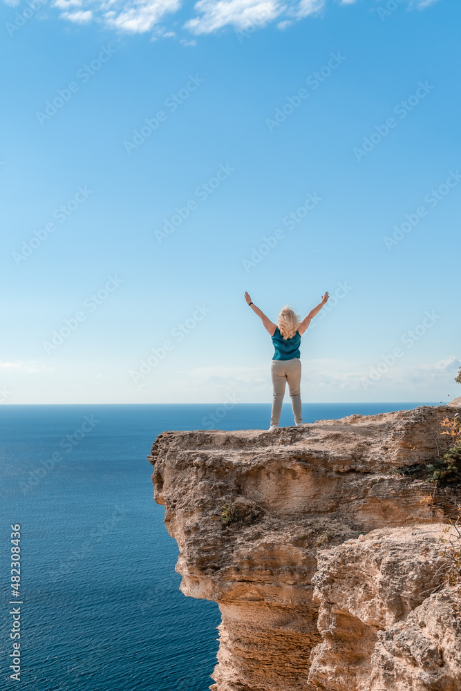The woman at the top of the mountain raised her hands up on blue sky background. The woman climbed to the top and enjoyed her success. Back view. The woman at the top of the mountain raised her hands up on blue sky background. The woman climbed to the top and enjoyed her success. Back view.