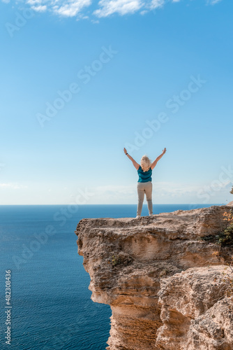 The woman at the top of the mountain raised her hands up on blue sky background. The woman climbed to the top and enjoyed her success. Back view.