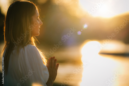 Sunset Meditation. Woman Meditating by the Lake in Prayer Position.