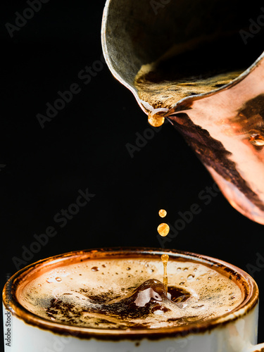 Espresso details. Close-up of pouring coffee into a white cup from a coffee pot, selective focus. The concept of making coffee in a bar, pub or restaurant. Brewing coffee in a cezve.