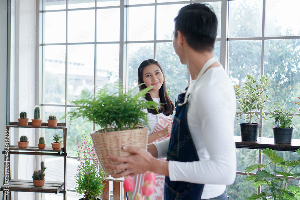 Happy Asian young couple in apron smiling at each other as they look after plants in greenhouse at home Happy Asian young couple in apron smiling at each other as they look after plants in greenhouse at home