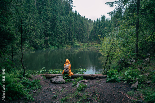 woman hiker with backpack in yellow raincoat looking at mountain lake
