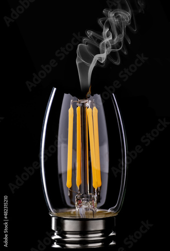 A classic Edison light bulb on a black background. The incandescent bulb explodes with fire and smoke