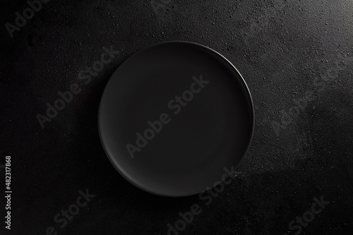 Empty black plate on black textured background. Moody, top down view.